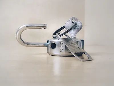 An unlocked silver padlock with a key inserted laying on a neutral surface.