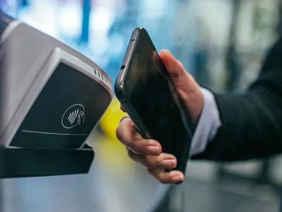 A hand holding a smartphone up to a tap to pay POS.